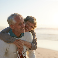 Portrait of happy mature man being embraced by his wife at the beach. Senior couple having fun at the sea shore.