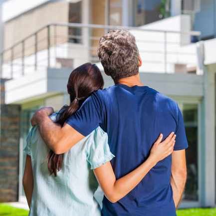 couple embracing in front of new big modern house, outdoor rear view back looking at their dream home